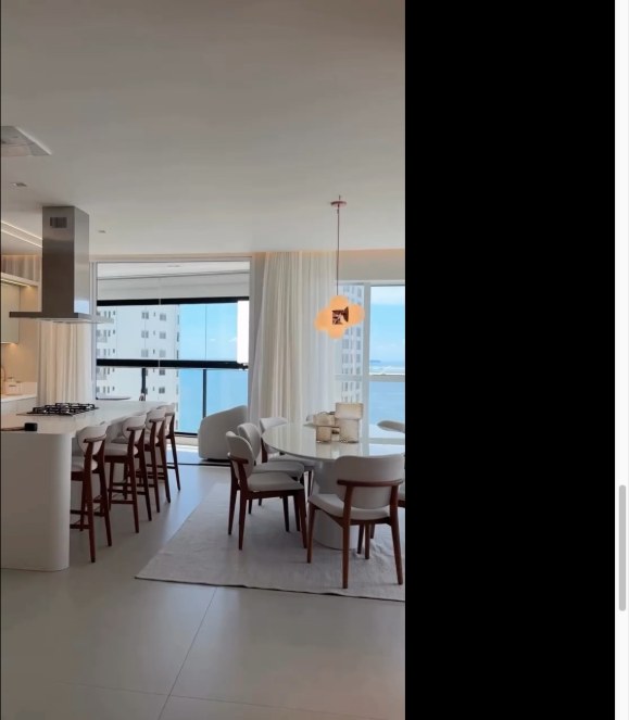 Cozinha com ilha branca, banquetas de madeira e vista para o mar
