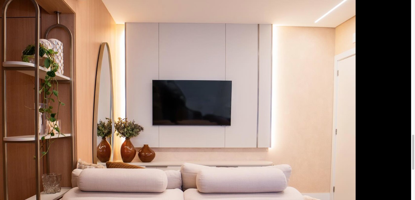 Living planejado com painel branco iluminado, estante em madeira e sofá claro